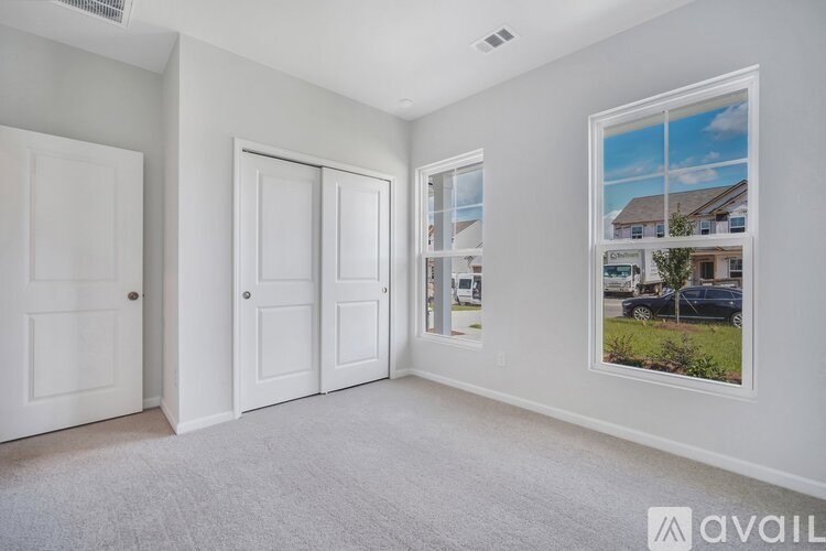 A room with white walls and carpeted floor with a picture of a house on the wall.