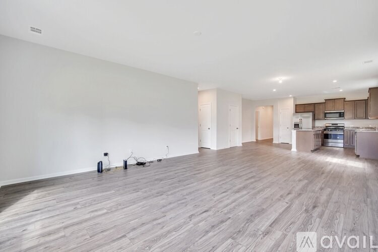 A spacious room with wooden flooring and a kitchen area in the background.