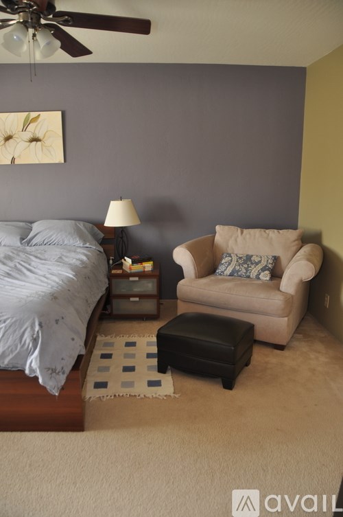 A bedroom with a bed, chair, and ceiling fan.