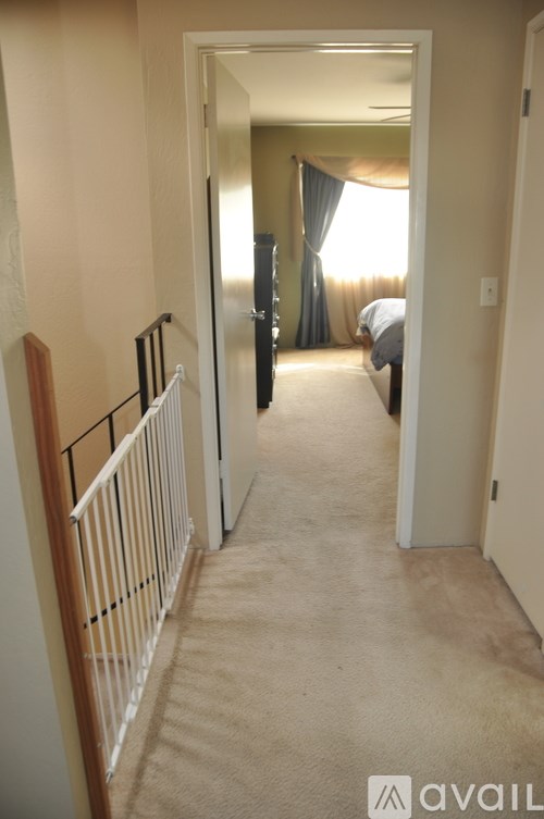 A hallway with a carpeted floor and a white railing on the left side leading to a bedroom.
