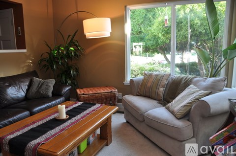 A living room with a black leather couch, a wooden coffee table with a candle on it, and a beige sofa with striped pillows.