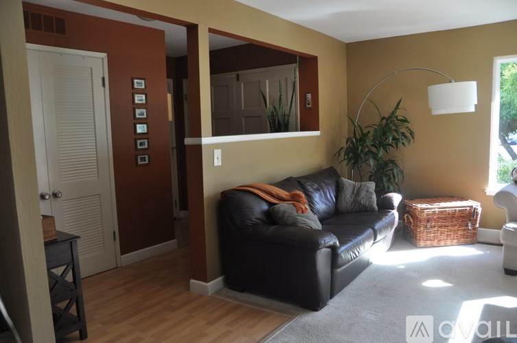 A living room with a black leather couch and a wooden floor.