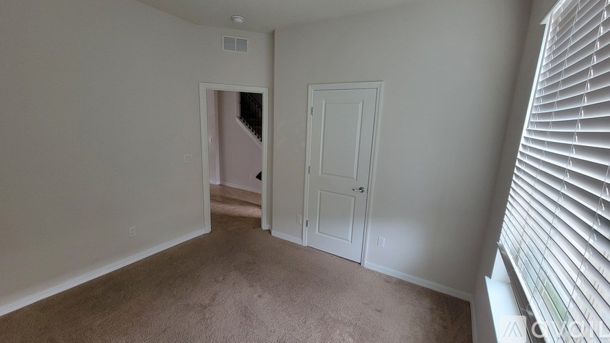 A room with a carpeted floor, a door, and a window with blinds.