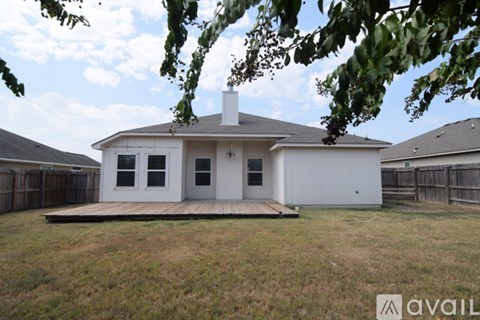 A white house with a porch and a chimney is surrounded by a fence and trees.