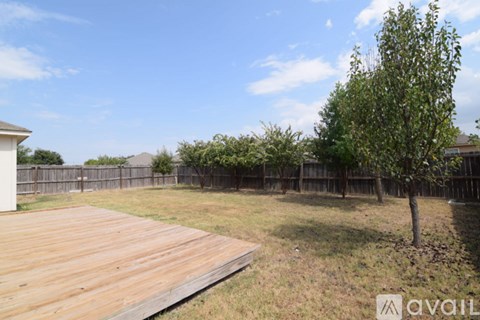 A wooden deck in the foreground with a tree and a fence in the background.
