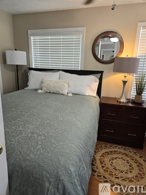 A bedroom with a bed, nightstand, and a round mirror on the wall.