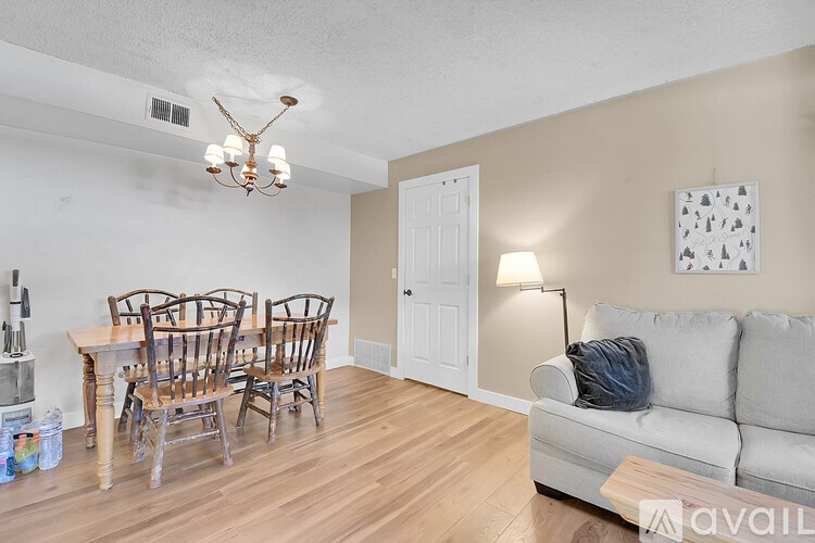 A living room with a grey couch, wooden chairs, and a chandelier.