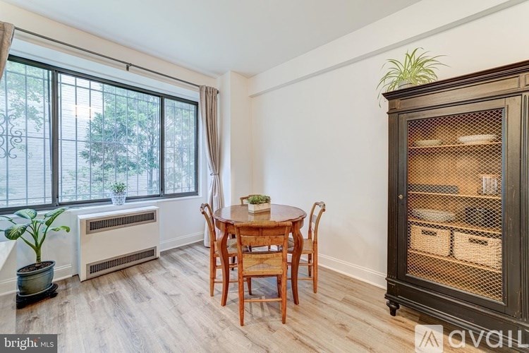 A dining room with a wooden table and chairs, a window with a view of trees, and a cabinet with glass doors.