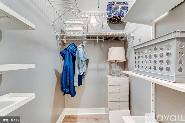 A small, white, and organized walk-in closet with a fan and a lamp.