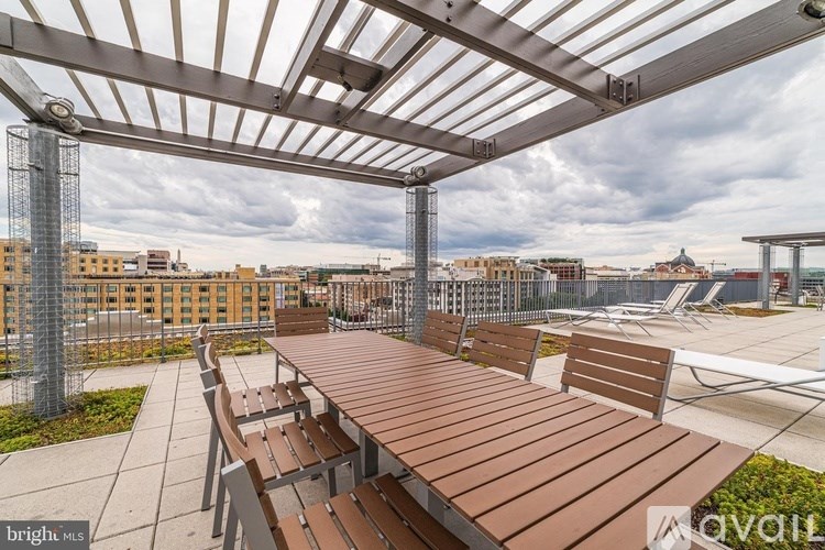 A wooden table and chairs are set up under a metal pergola.