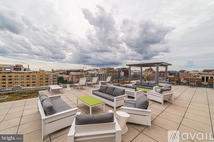A rooftop patio with white furniture and a cloudy sky in the background.