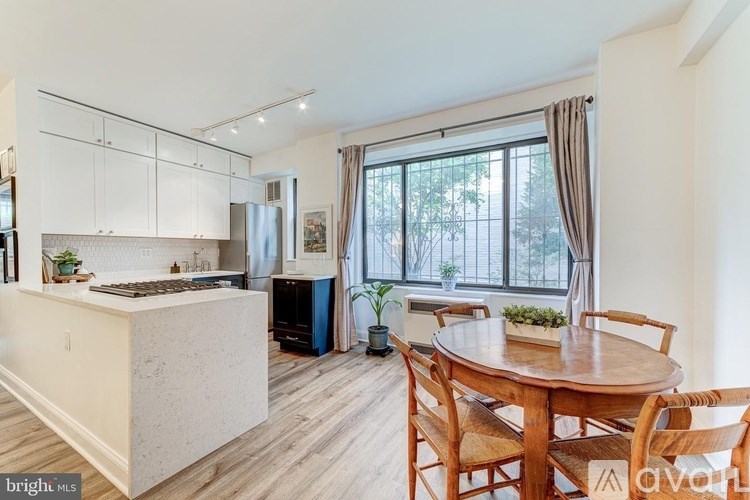 A kitchen with a dining table and chairs in the foreground and a window with a view of trees in the background.