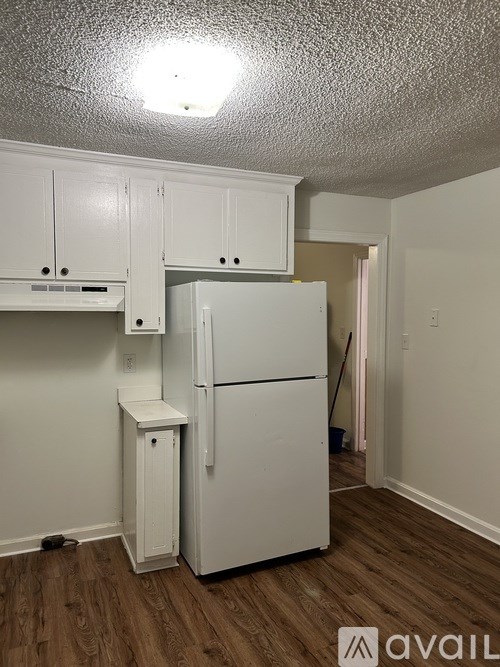A white refrigerator in a kitchen with wooden floors and white cabinets.