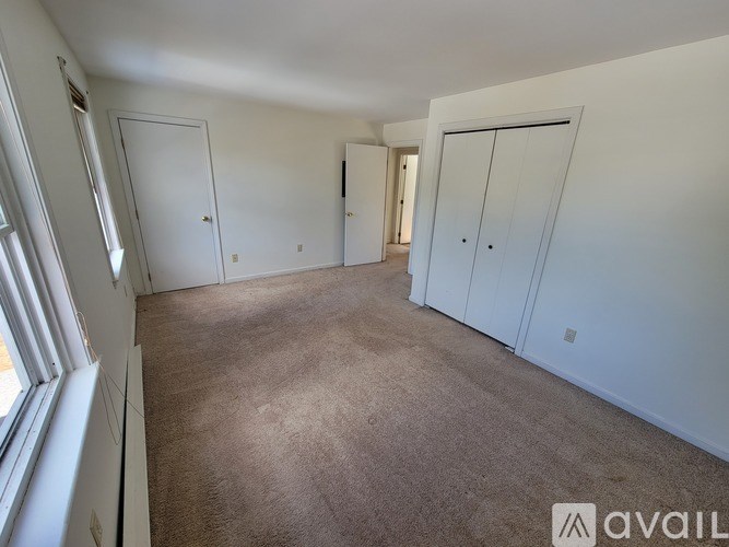 A room with white walls and carpeted floor with three doors.
