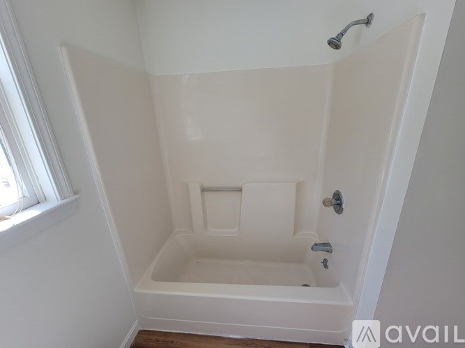 A white bathtub with a shower head and a window.