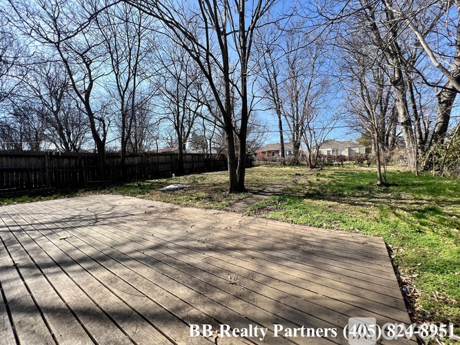 A wooden deck leads to a grassy area with trees and a fence in the background.