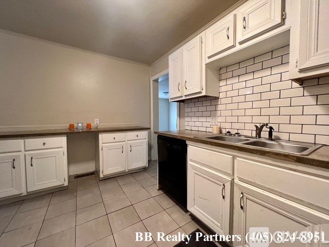 A kitchen with white cabinets and a black dishwasher.