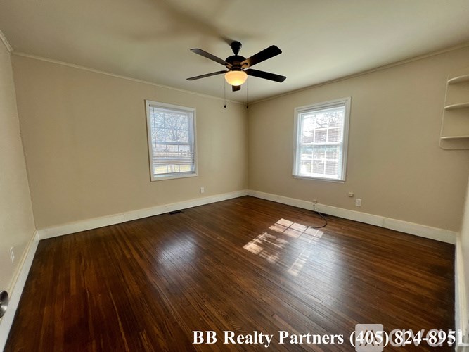 A room with a ceiling fan and two windows.