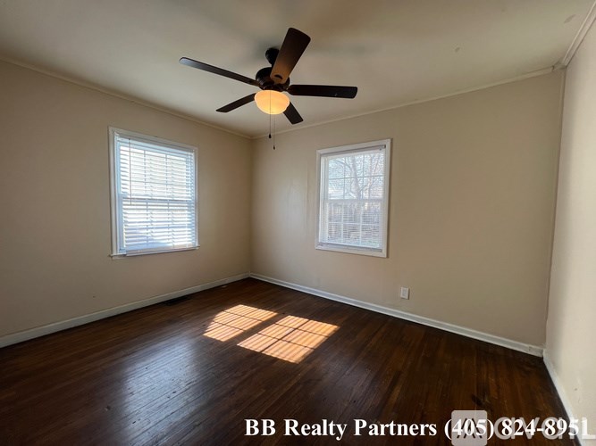 A room with a ceiling fan and two windows.