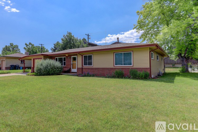 A house with a red roof and a brown wall is surrounded by a green lawn.