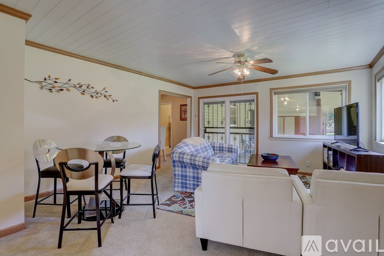 A living room with a white couch, a glass table, and a ceiling fan.