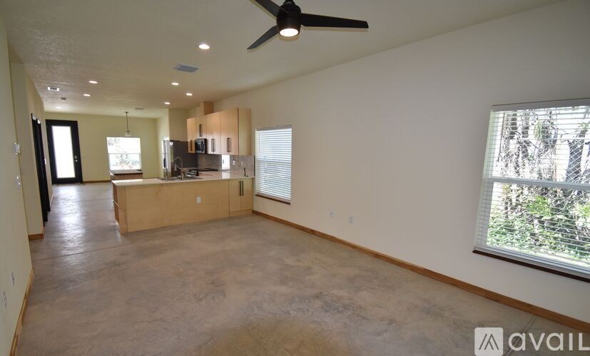 A spacious living room with a ceiling fan and a view of trees through the window.