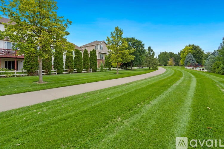 A grassy field with a pathway leading to a building with trees on either side.