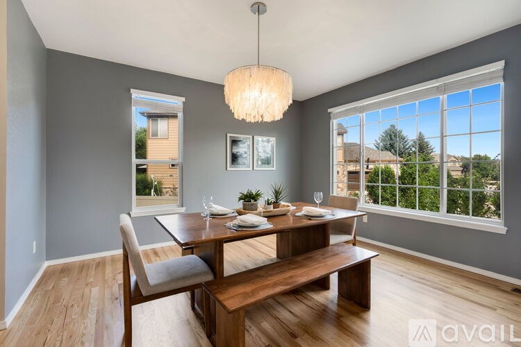 A dining room with a wooden table and bench, a chandelier, and a view of the outdoors through the windows.