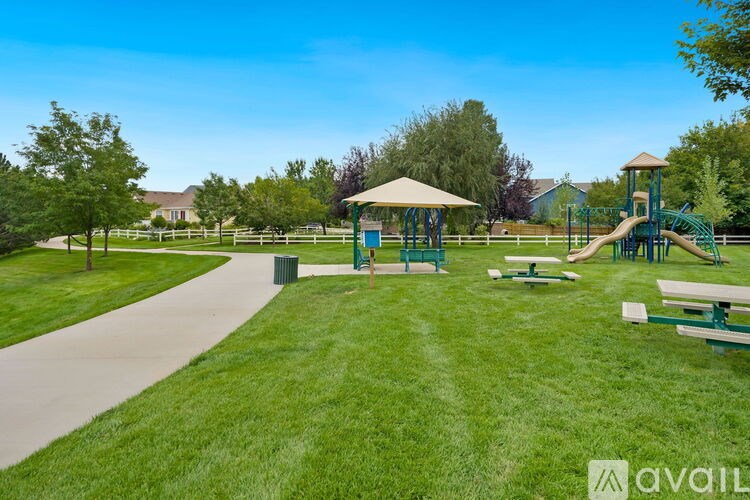 A playground with a slide, swings, and a picnic table is surrounded by a grassy area and trees.