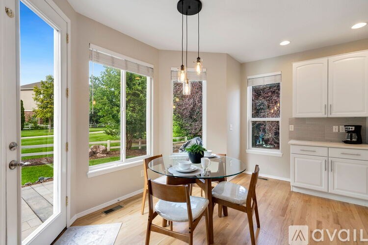 A dining room with a glass table and chairs, a hanging light fixture, and a view of a backyard through the window.