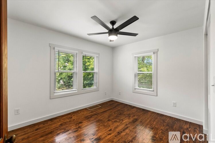 A room with a ceiling fan and two windows.