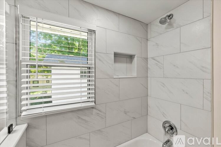 A bathroom with a window covered by white blinds.