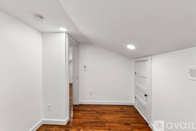 A white room with wooden floors and a doorway leading to another room.