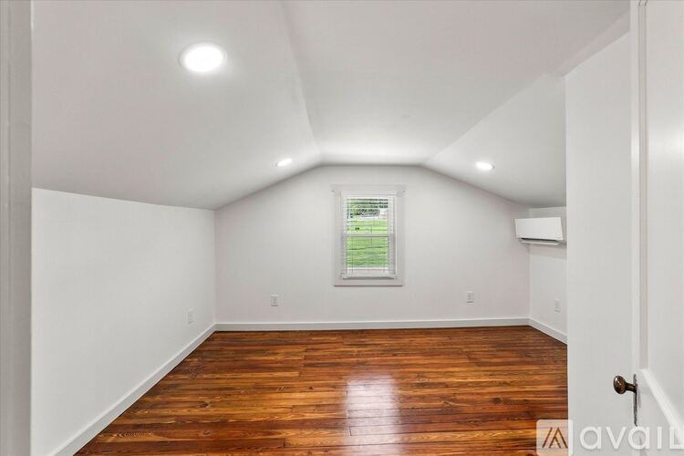 A room with wooden floors and white walls, with a window and a door visible.