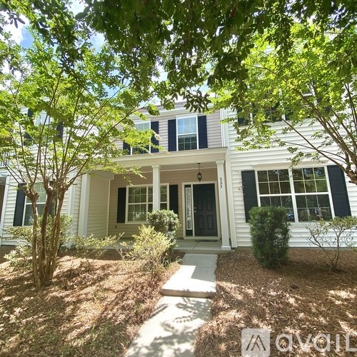 A white house with a black door and windows surrounded by trees.