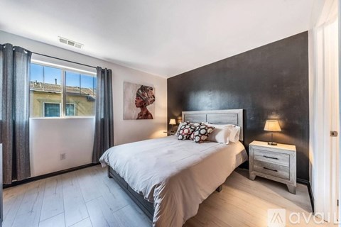 A bedroom with a large bed, a nightstand, and a window with curtains.