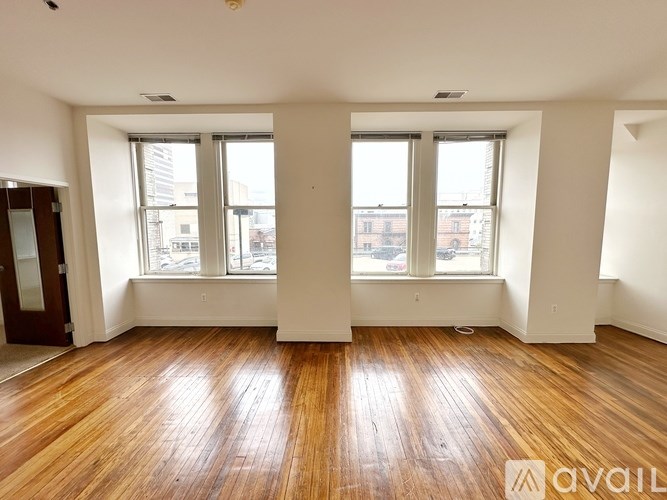 A room with wooden floors and white walls, with two windows and a door on the left side.