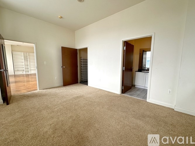 A spacious room with beige carpeting and white walls, featuring a sliding glass door and a wooden door.