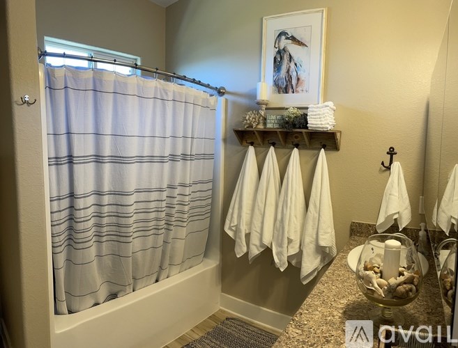 A bathroom with a shower curtain, towels, and a candle on a shelf.