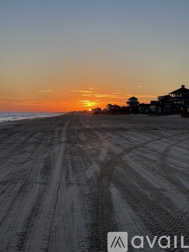 A beach at sunset with tire tracks in the sand.