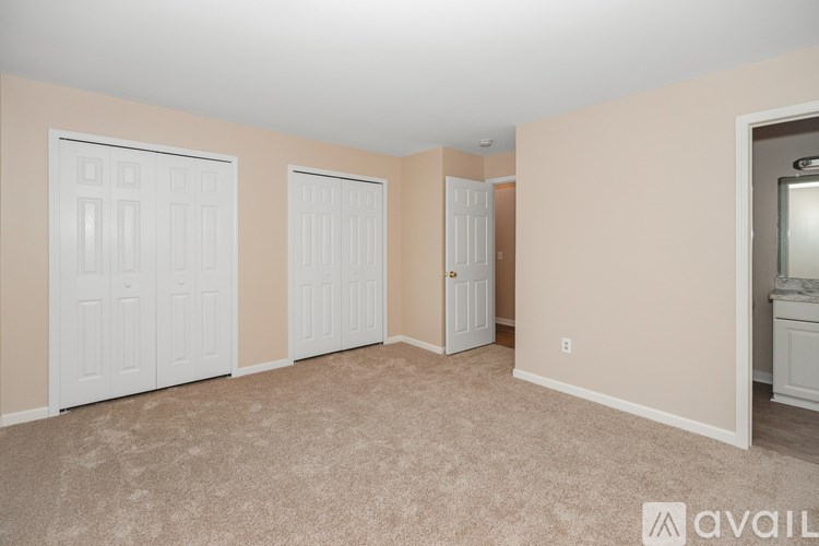 A room with beige walls and carpeted floor with three white doors.