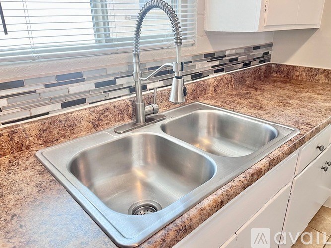 A kitchen sink with a chrome faucet and a brown granite countertop.