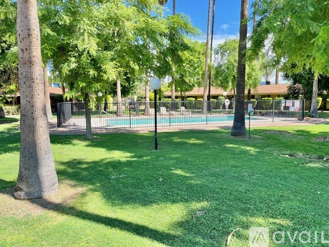 A grassy area with trees and a pool in the background.