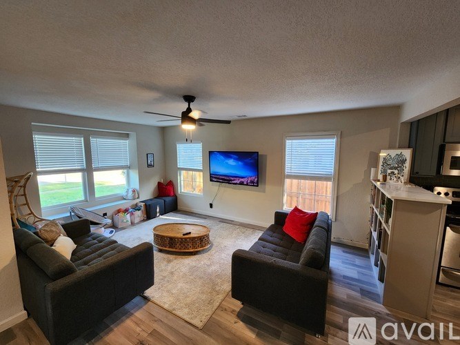 A living room with a black couch, a flat screen TV, and a ceiling fan.