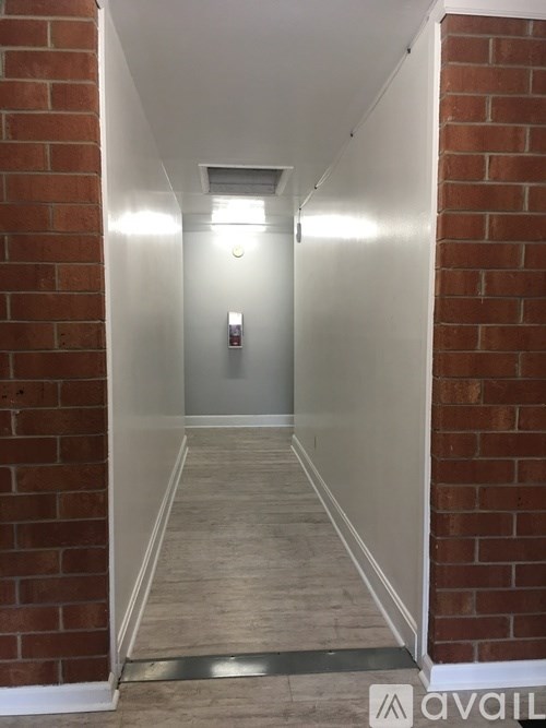 A long hallway with a brick wall on the side and a white door at the end.