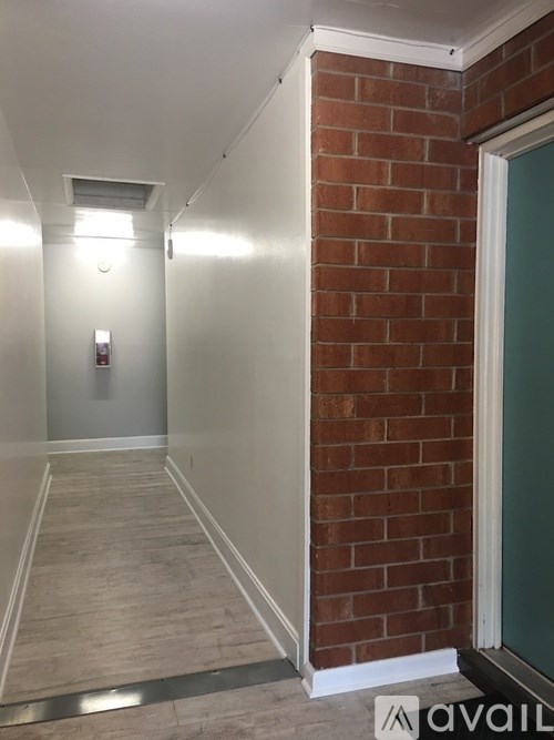 A long hallway with a brick wall on the side and a door on the other.