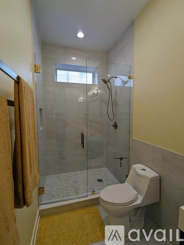 A bathroom with a toilet, a glass shower stall, and a towel hanging on the door.