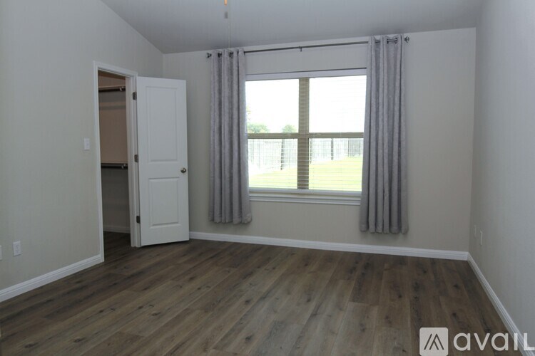 A room with a wooden floor and a large window with curtains.