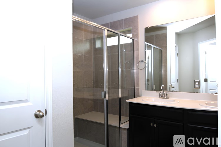 A bathroom with a white door, a glass shower stall, and a vanity with a mirror.