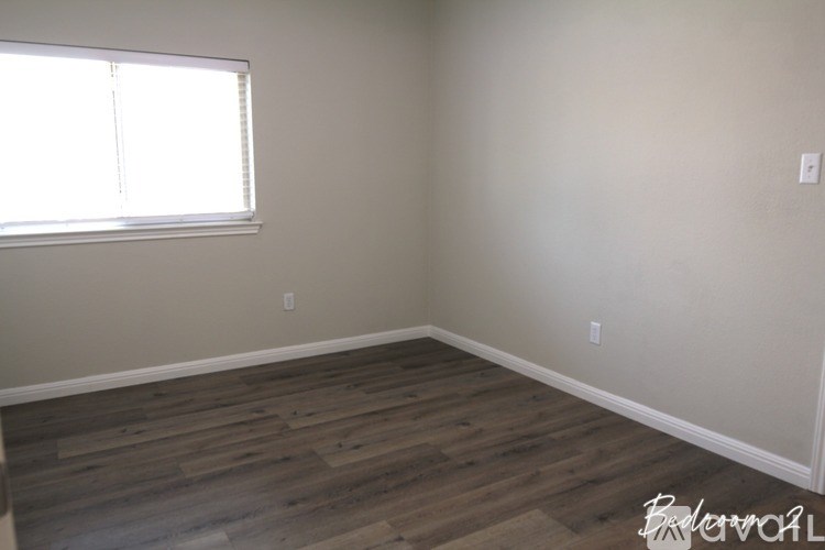 A room with wooden flooring and a window letting in sunlight.